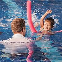 A young girl being coached how to swim by an instructor. 